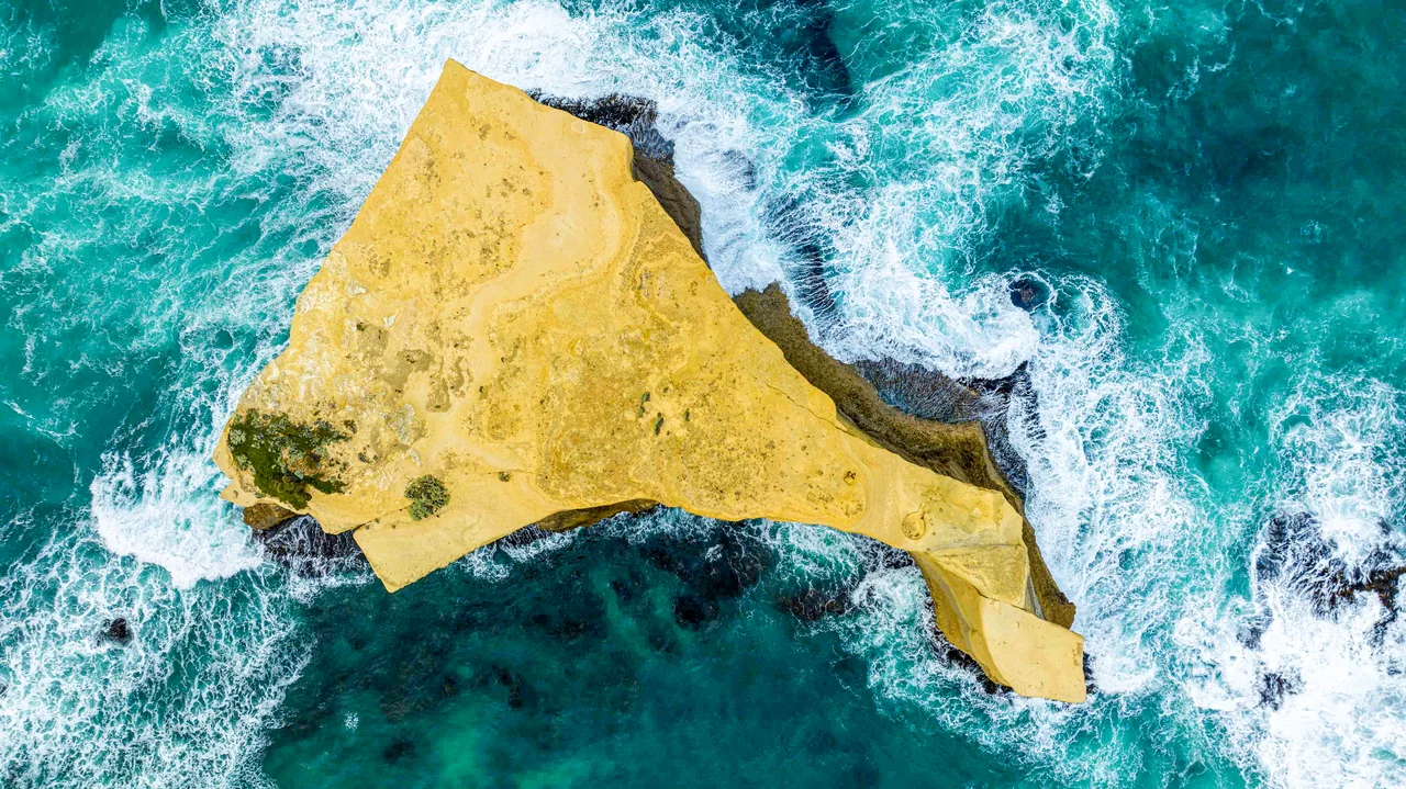 Aerial view of a rock island surrounded by surf